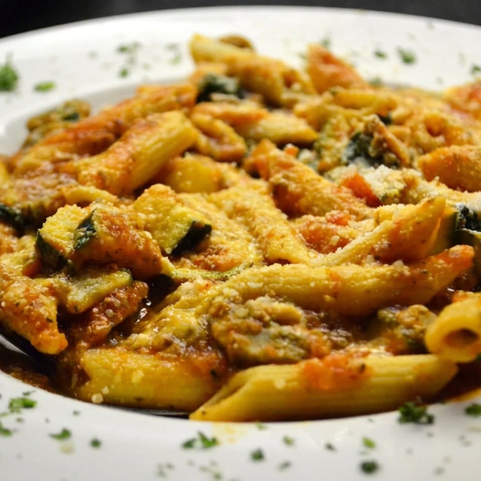 Plate of baked pasta with vegetables, tomato sauce, melted cheese, breadcrumbs, and herbs, served with a spoon.