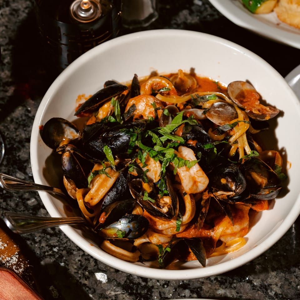 Seafood pasta with shrimp, mussels, clams, tomato sauce, and herbs served alongside red wine and garlic bread.