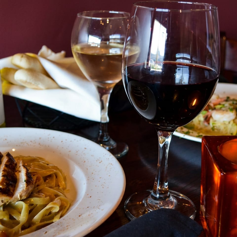 Restaurant table featuring creamy chicken pasta, shrimp dish, red and white wine, bread, and a glowing candle.
