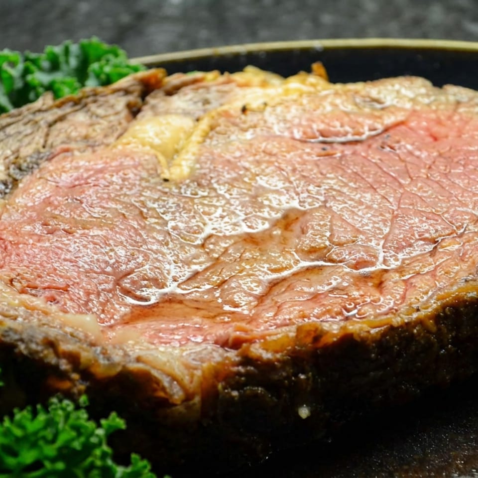 Thick medium-rare steak with a browned crust, glistening juices, and curly parsley garnish on a dark plate.